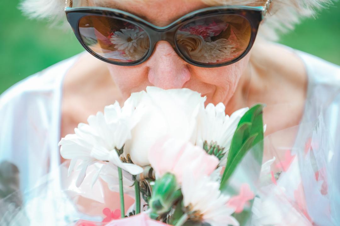 Personne âgée avec lunettes de soleil respirant des fleurs d'été